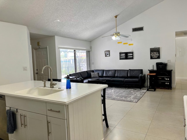 kitchen with sink, a textured ceiling, vaulted ceiling, light tile patterned flooring, and a kitchen island with sink