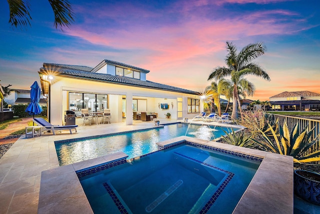 pool at dusk with an in ground hot tub and a patio