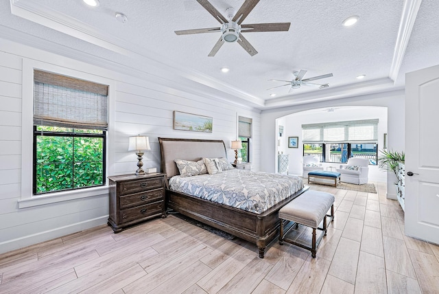 bedroom with a textured ceiling, ceiling fan, a tray ceiling, and ornamental molding