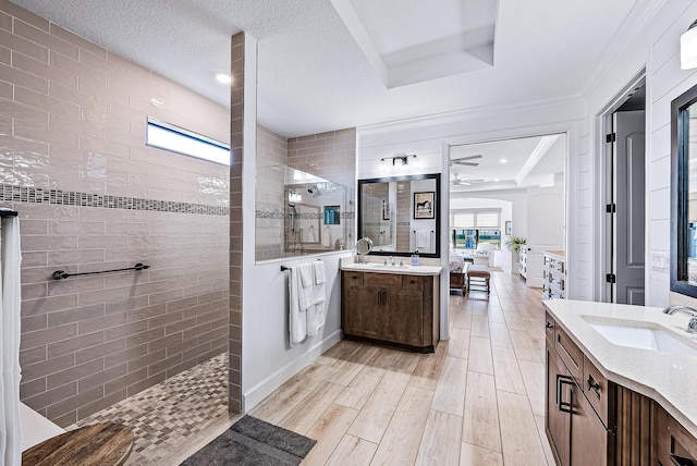 bathroom featuring a textured ceiling, tiled shower, ornamental molding, vanity, and a tray ceiling