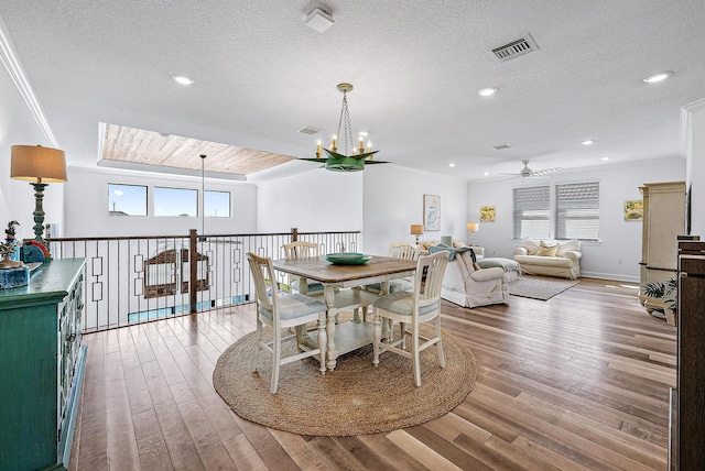 dining space featuring ceiling fan with notable chandelier, a textured ceiling, and light hardwood / wood-style flooring