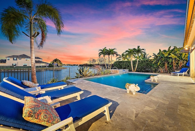 pool at dusk featuring pool water feature, a water view, and a patio area