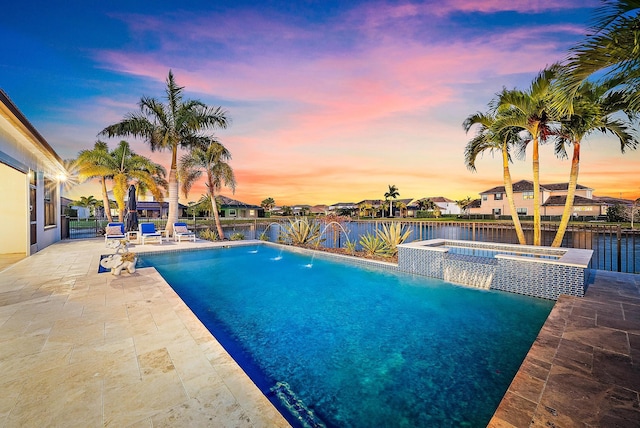 pool at dusk with a patio area, pool water feature, an in ground hot tub, and a water view