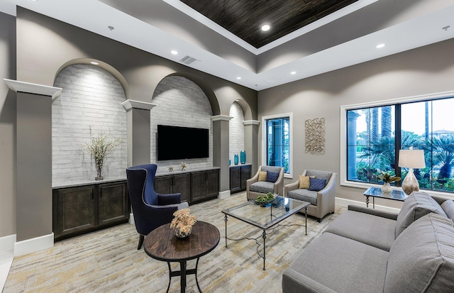 living room featuring ornate columns, a high ceiling, ornamental molding, and a tray ceiling