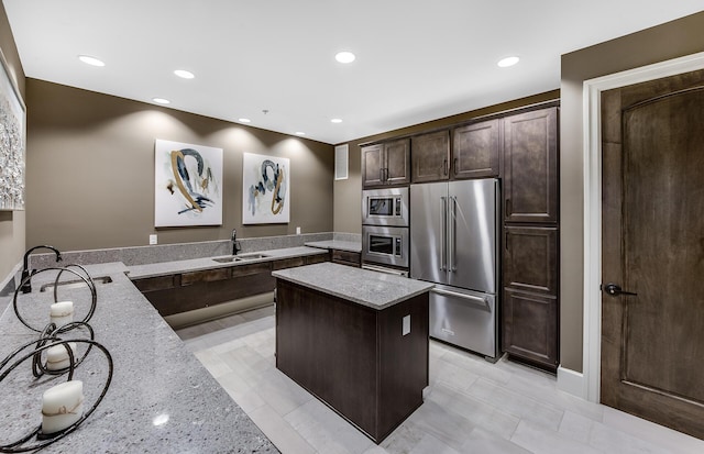 kitchen featuring stainless steel appliances, sink, light stone counters, and kitchen peninsula