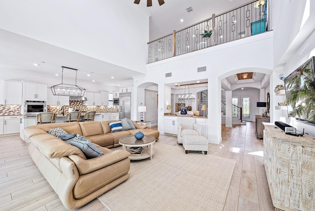 living room with a high ceiling, light wood-type flooring, and ceiling fan with notable chandelier