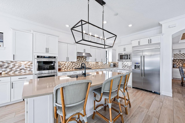 kitchen featuring white cabinets, decorative light fixtures, built in appliances, and a center island with sink