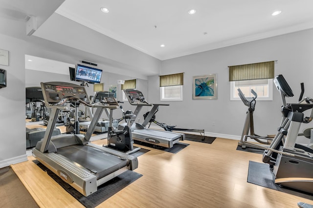 exercise room with ornamental molding and light wood-type flooring