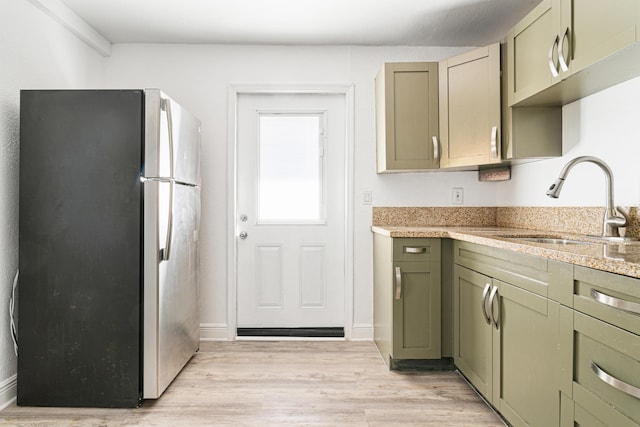 kitchen featuring sink, green cabinetry, light hardwood / wood-style floors, and stainless steel fridge