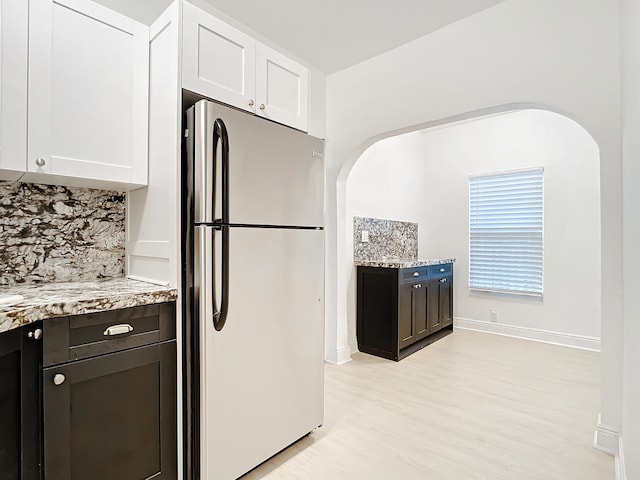 kitchen featuring white cabinets, stainless steel refrigerator, tasteful backsplash, and light stone counters