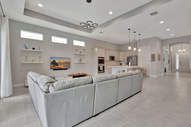 tiled living room with sink, a tray ceiling, and a notable chandelier