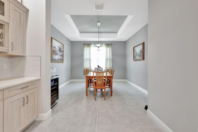 dining space with a raised ceiling, light tile patterned floors, wine cooler, and an inviting chandelier