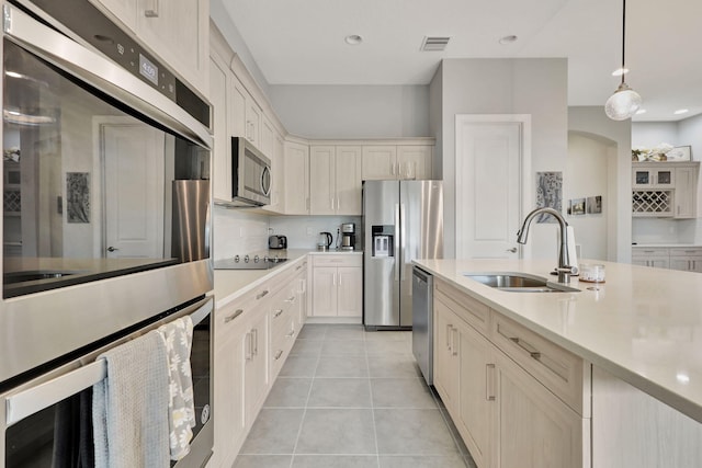 kitchen with light tile patterned floors, stainless steel appliances, backsplash, decorative light fixtures, and sink