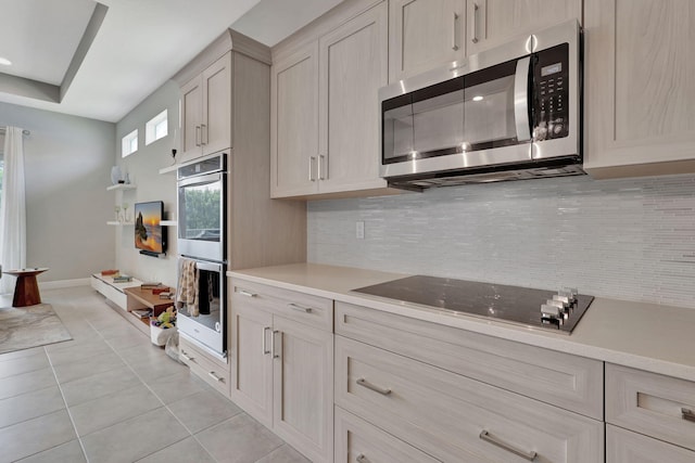 kitchen with multiple ovens, light tile patterned floors, black electric stovetop, tasteful backsplash, and light brown cabinetry