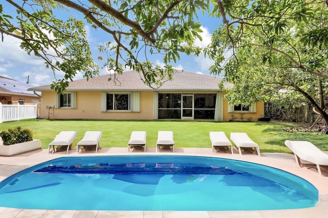 back of house with an outdoor pool, a lawn, fence, and stucco siding