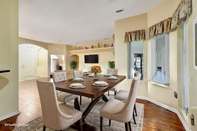 dining space featuring arched walkways, wood-type flooring, visible vents, and baseboards