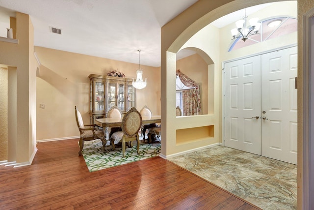 entryway featuring baseboards, visible vents, arched walkways, hardwood / wood-style flooring, and a chandelier