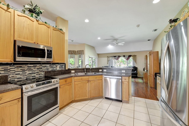 kitchen with dark countertops, appliances with stainless steel finishes, a peninsula, a sink, and backsplash