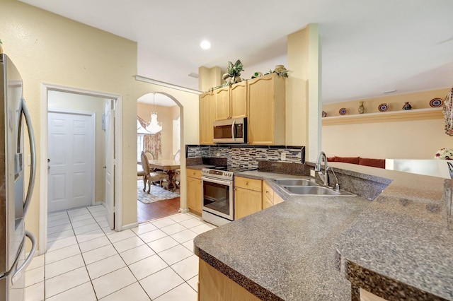 kitchen featuring arched walkways, stainless steel appliances, light brown cabinetry, and a sink