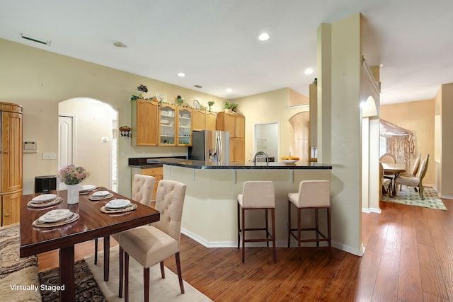 kitchen with arched walkways, wood finished floors, stainless steel fridge, and glass insert cabinets