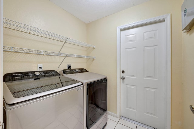 clothes washing area featuring laundry area, baseboards, a textured ceiling, washing machine and dryer, and light tile patterned flooring