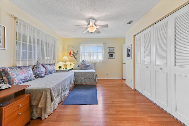 bedroom with a textured ceiling, a closet, ceiling fan, and light hardwood / wood-style floors