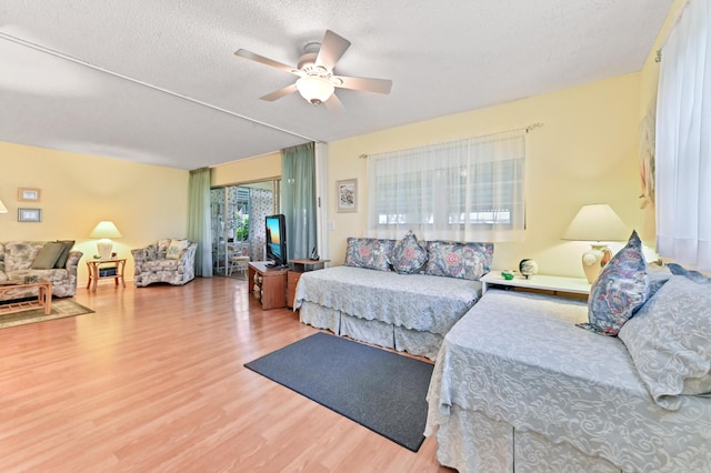 living room featuring ceiling fan, light wood-type flooring, and a textured ceiling