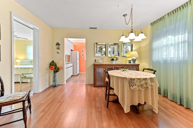 dining area with a textured ceiling, light hardwood / wood-style flooring, and ceiling fan with notable chandelier