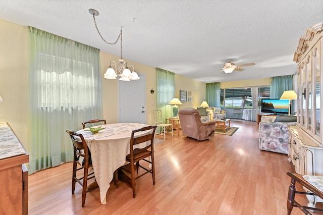 dining area featuring a textured ceiling, light hardwood / wood-style floors, and ceiling fan with notable chandelier