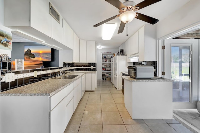 kitchen with decorative backsplash, kitchen peninsula, sink, light tile patterned floors, and white cabinetry