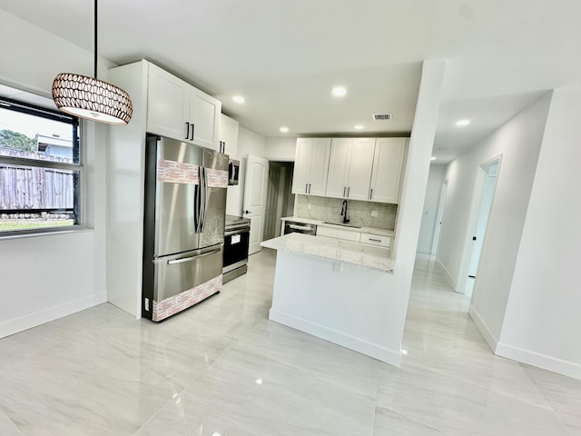 kitchen featuring light stone countertops, white cabinets, appliances with stainless steel finishes, decorative light fixtures, and sink