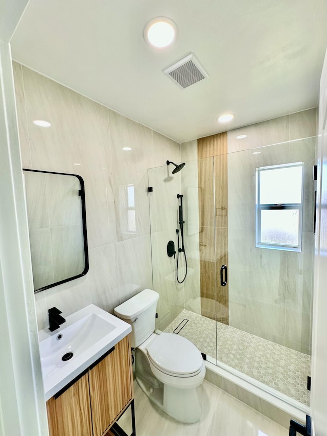 bathroom featuring toilet, tile walls, a shower with shower door, and vanity