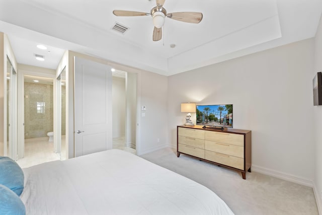 bedroom featuring a tray ceiling, ceiling fan, light colored carpet, and ensuite bathroom