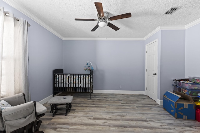 bedroom featuring a textured ceiling, ceiling fan, ornamental molding, wood-type flooring, and a nursery area