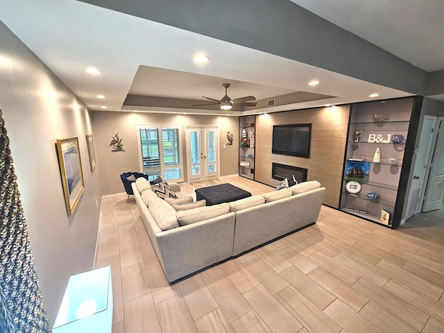 living room with ceiling fan, a large fireplace, french doors, and a tray ceiling