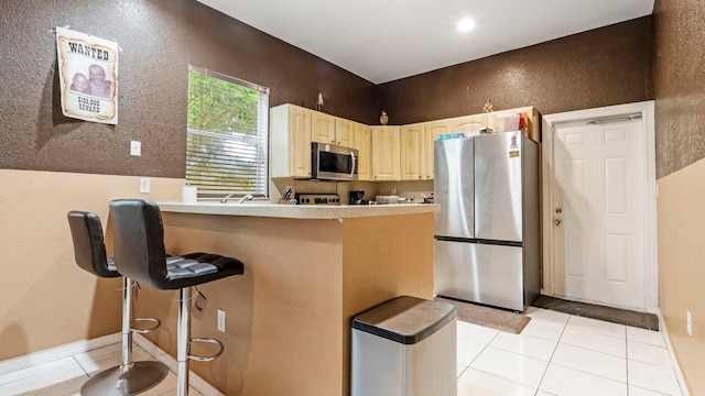 kitchen featuring a kitchen breakfast bar, kitchen peninsula, light tile patterned floors, and appliances with stainless steel finishes