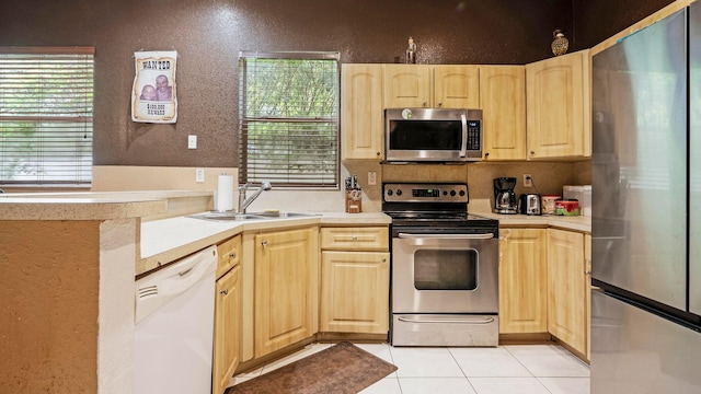 kitchen featuring sink, kitchen peninsula, light brown cabinetry, light tile patterned floors, and appliances with stainless steel finishes