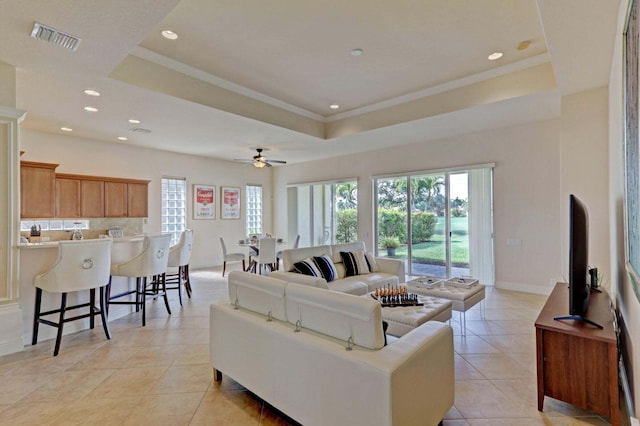 living room featuring ceiling fan, light tile patterned floors, ornamental molding, and a tray ceiling