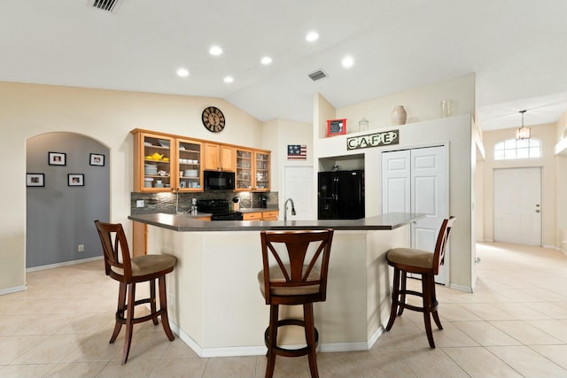 kitchen with lofted ceiling, tasteful backsplash, black appliances, and a breakfast bar