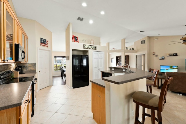 kitchen with a breakfast bar, ceiling fan, black appliances, an island with sink, and vaulted ceiling