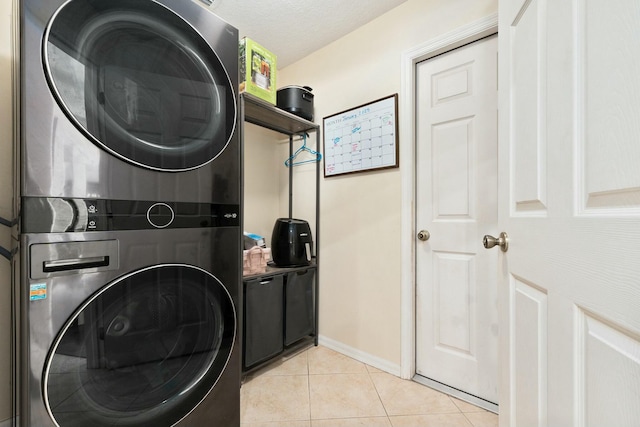 clothes washing area featuring stacked washer and dryer, light tile patterned floors, and a textured ceiling