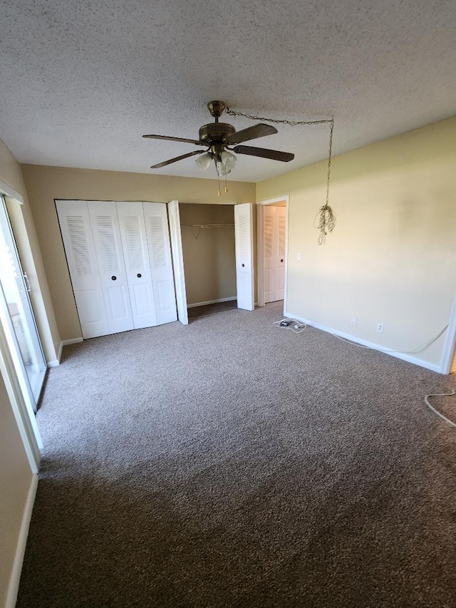 unfurnished bedroom featuring carpet, ceiling fan with notable chandelier, a textured ceiling, and two closets