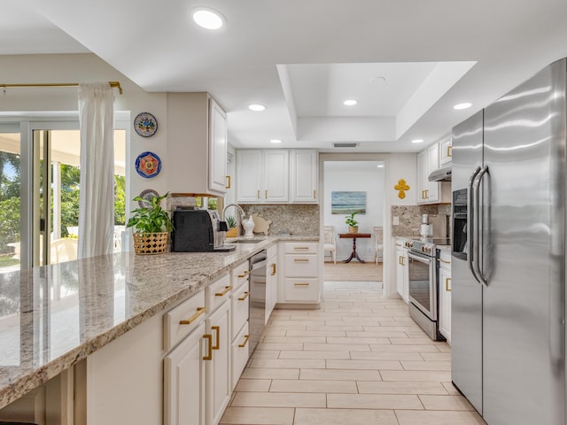 kitchen featuring appliances with stainless steel finishes, light stone countertops, white cabinets, decorative backsplash, and a raised ceiling