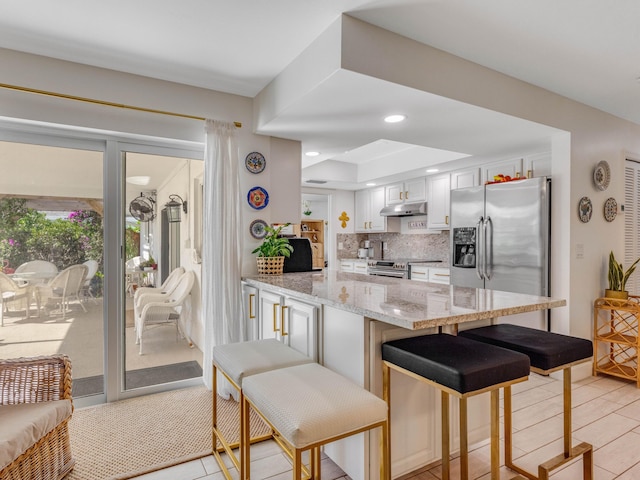 kitchen with appliances with stainless steel finishes, white cabinetry, a breakfast bar area, backsplash, and kitchen peninsula