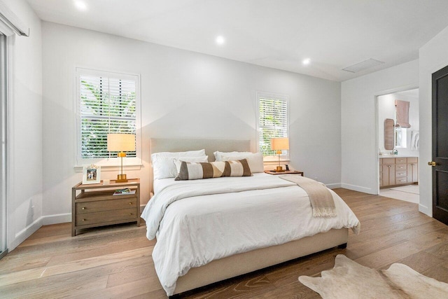 bedroom with multiple windows, connected bathroom, and light hardwood / wood-style flooring