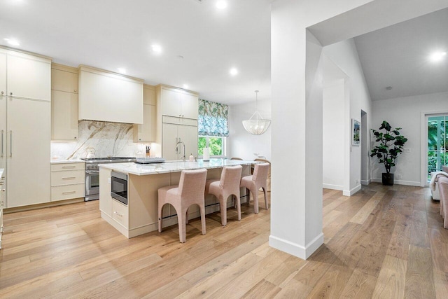 kitchen with an island with sink, built in appliances, backsplash, and cream cabinetry