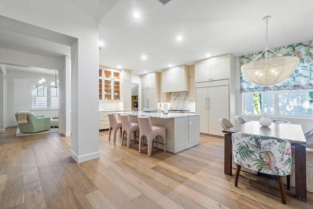 kitchen with pendant lighting, plenty of natural light, an island with sink, white cabinets, and light wood-type flooring