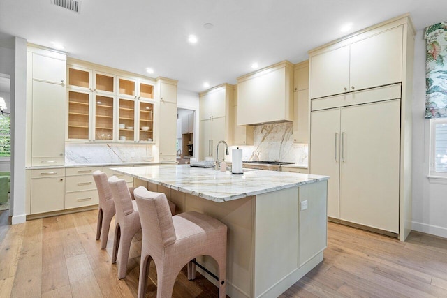 kitchen featuring an island with sink, light stone countertops, light wood-type flooring, and cream cabinetry