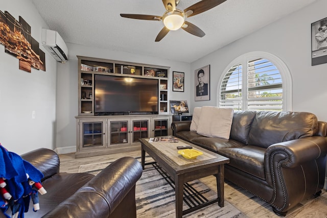 living room with ceiling fan, a wall unit AC, light hardwood / wood-style floors, and a textured ceiling