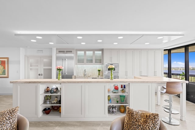 bar featuring floor to ceiling windows, multiple ovens, built in fridge, white cabinetry, and sink